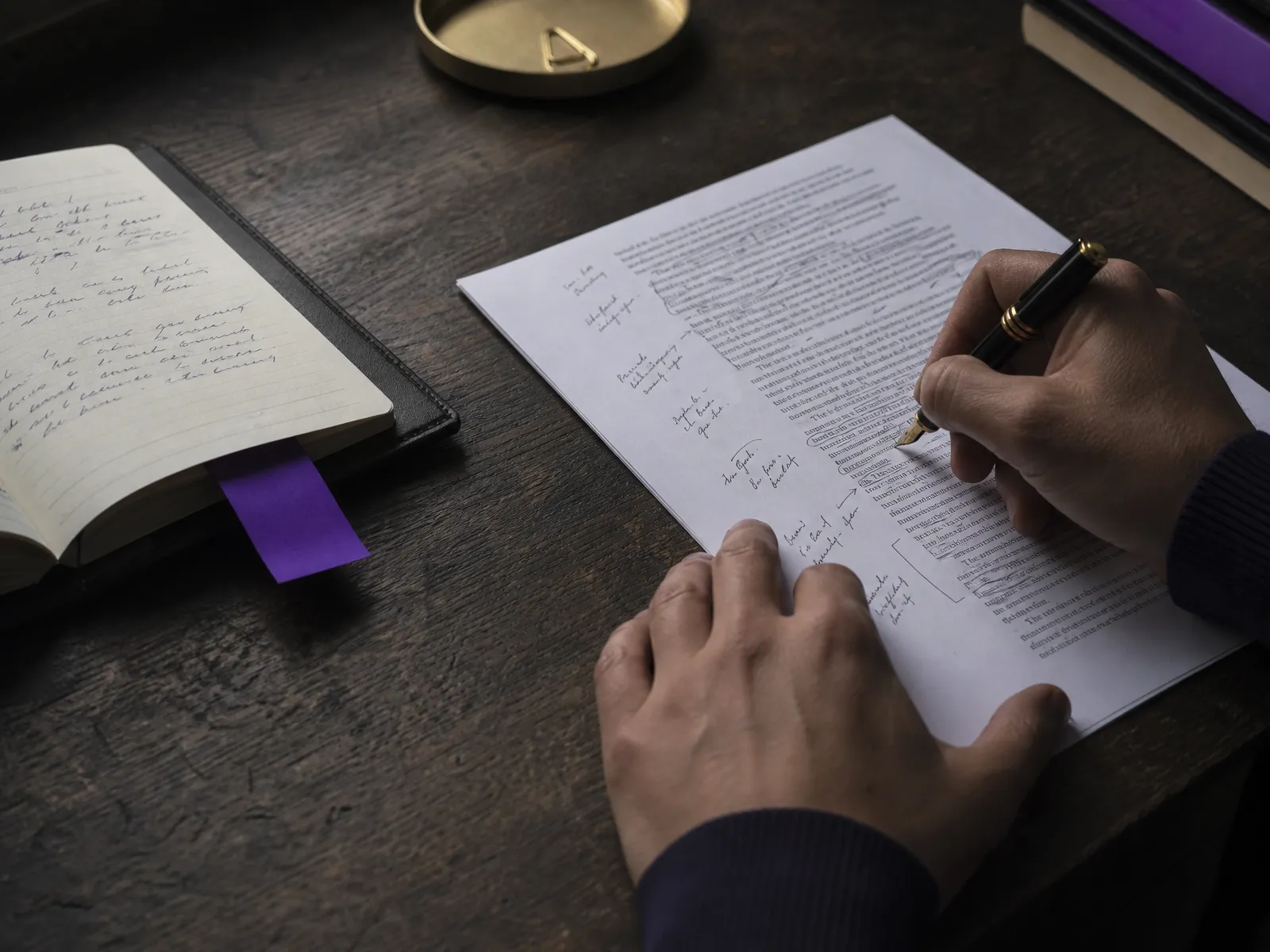 A hand annotating a printed page with a fountain pen next to a violet bookmark on a dark wooden desk, mapping links between posts.
