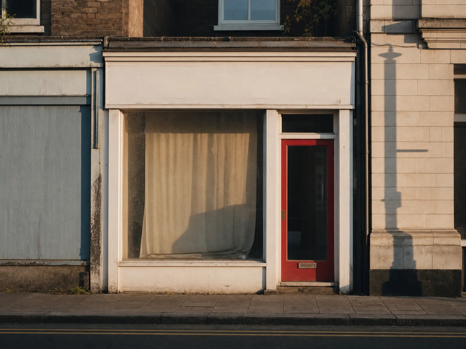 A small British shopfront with a red door and drawn curtains