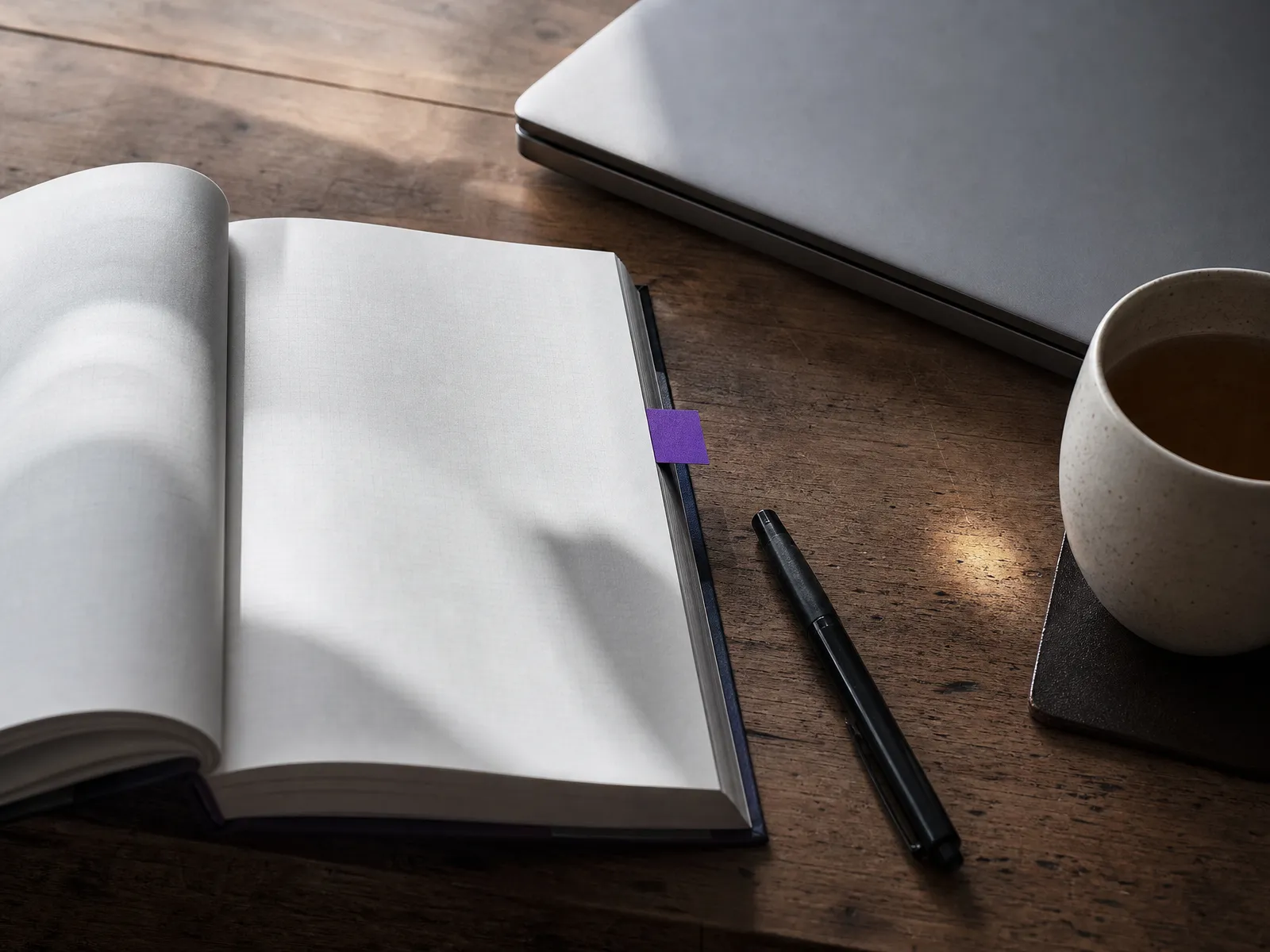 An open notebook and pen beside a closed laptop on a desk in soft daylight, illustrating questions to ask before paying for SEO.