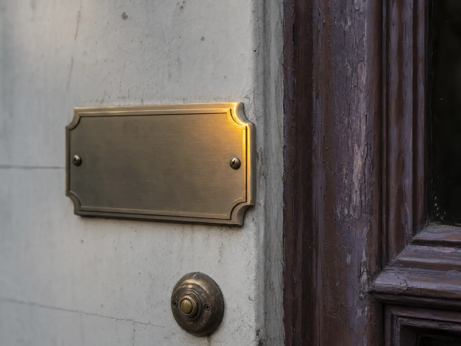 Blank polished brass nameplate beside a weathered red door on a small law office