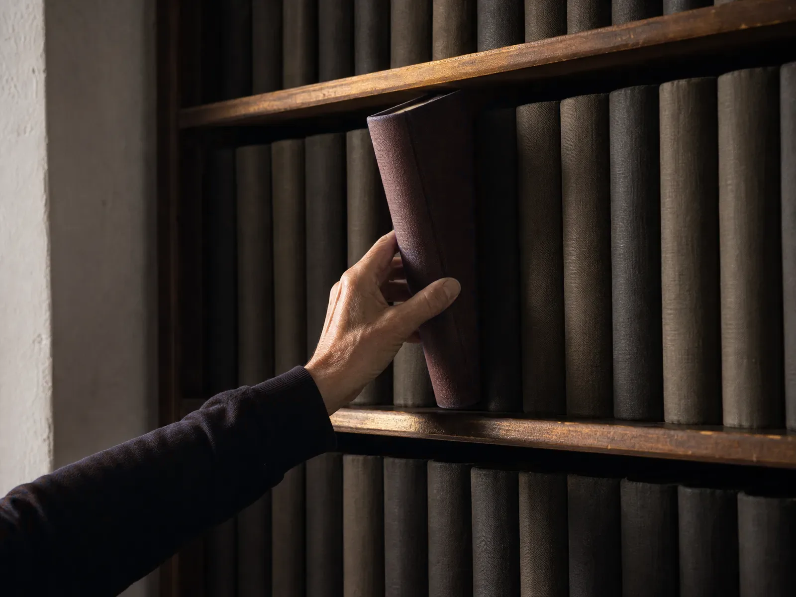 A hand lifting a red-spined volume from a shelf of old law reports in a quiet