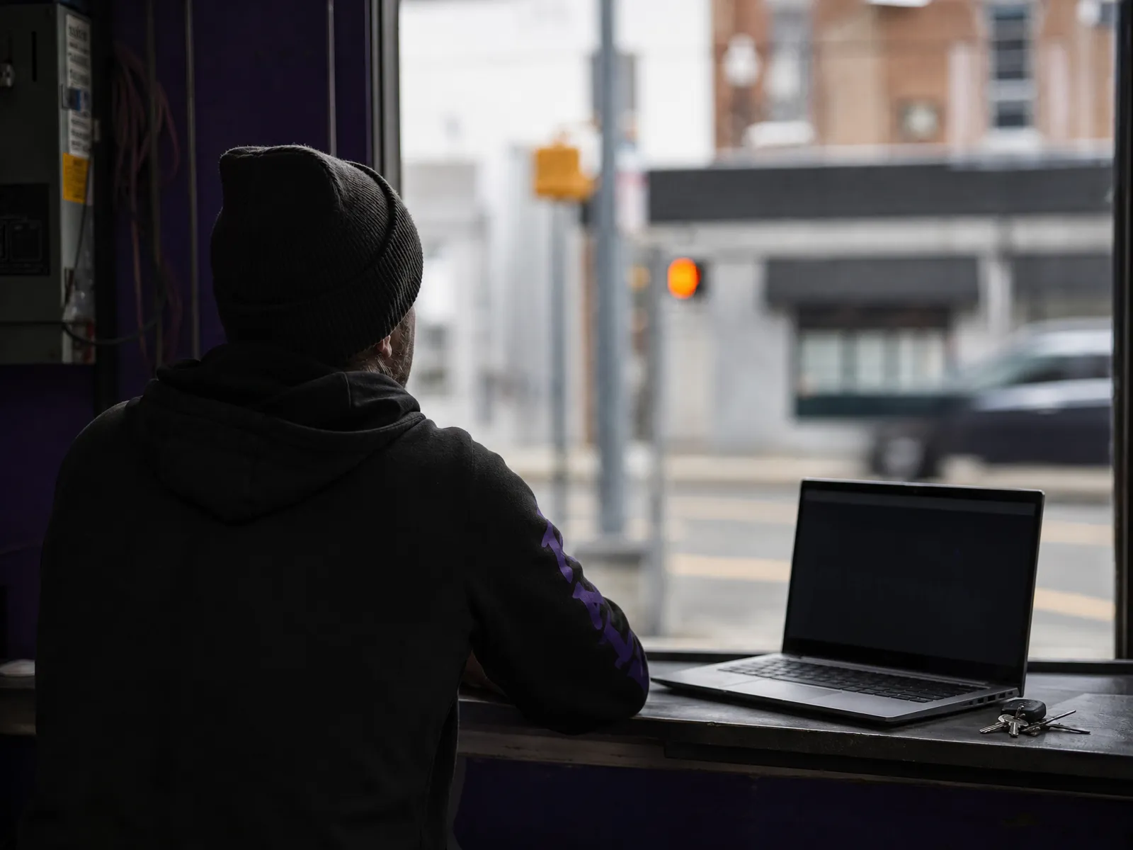 Inside a small electrical contractor's unit looking out to the street, an open laptop with a dark screen on the counter.