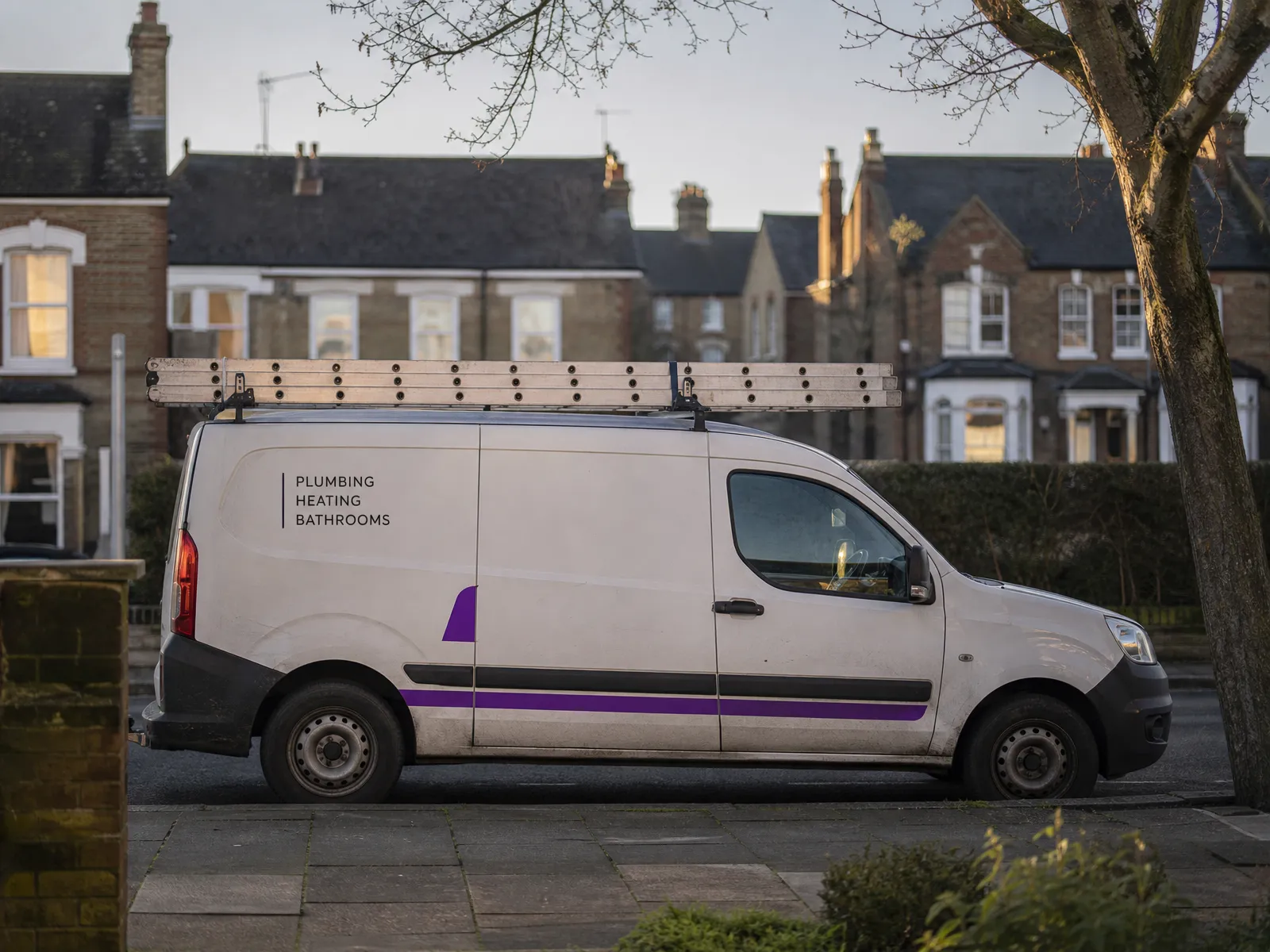 A sign-written trade van parked on a quiet UK residential street at golden hour.