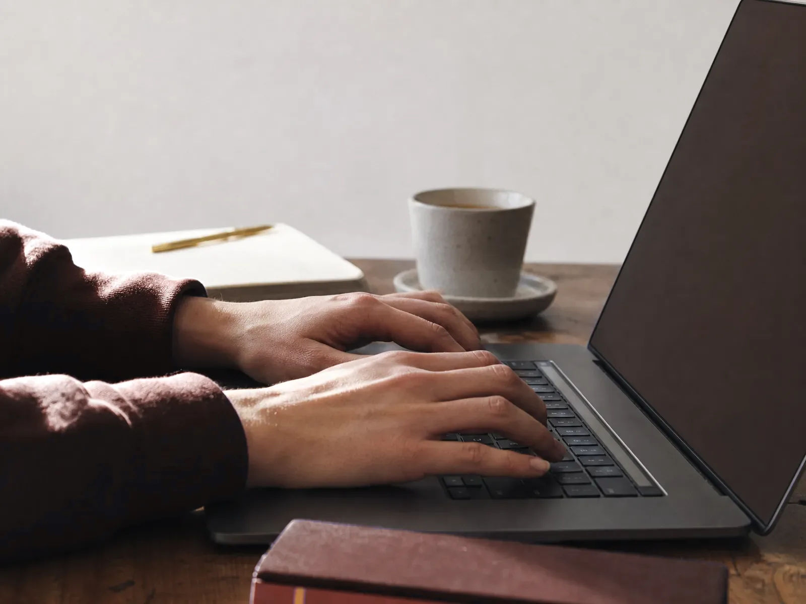 Hands resting on a laptop keyboard in soft daylight with a dark screen