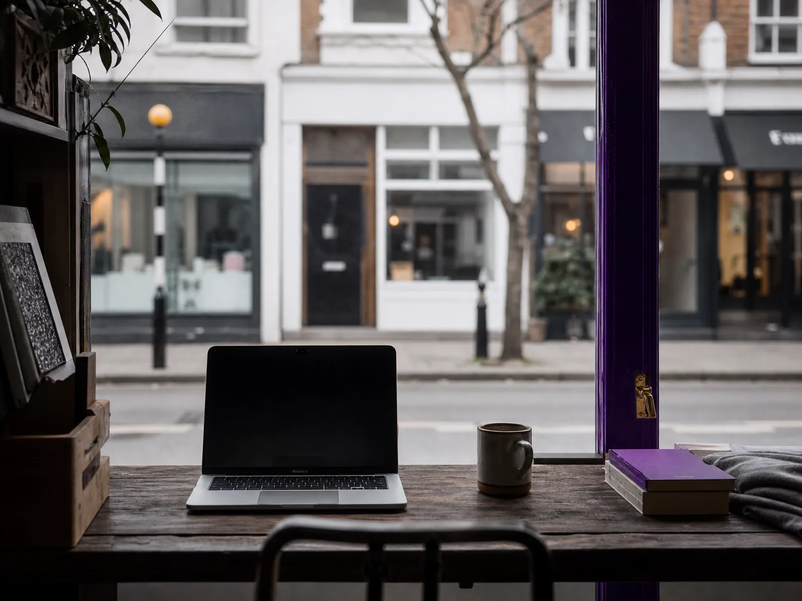 View from inside a small shop through the window onto a quiet UK high street, an open laptop on the counter