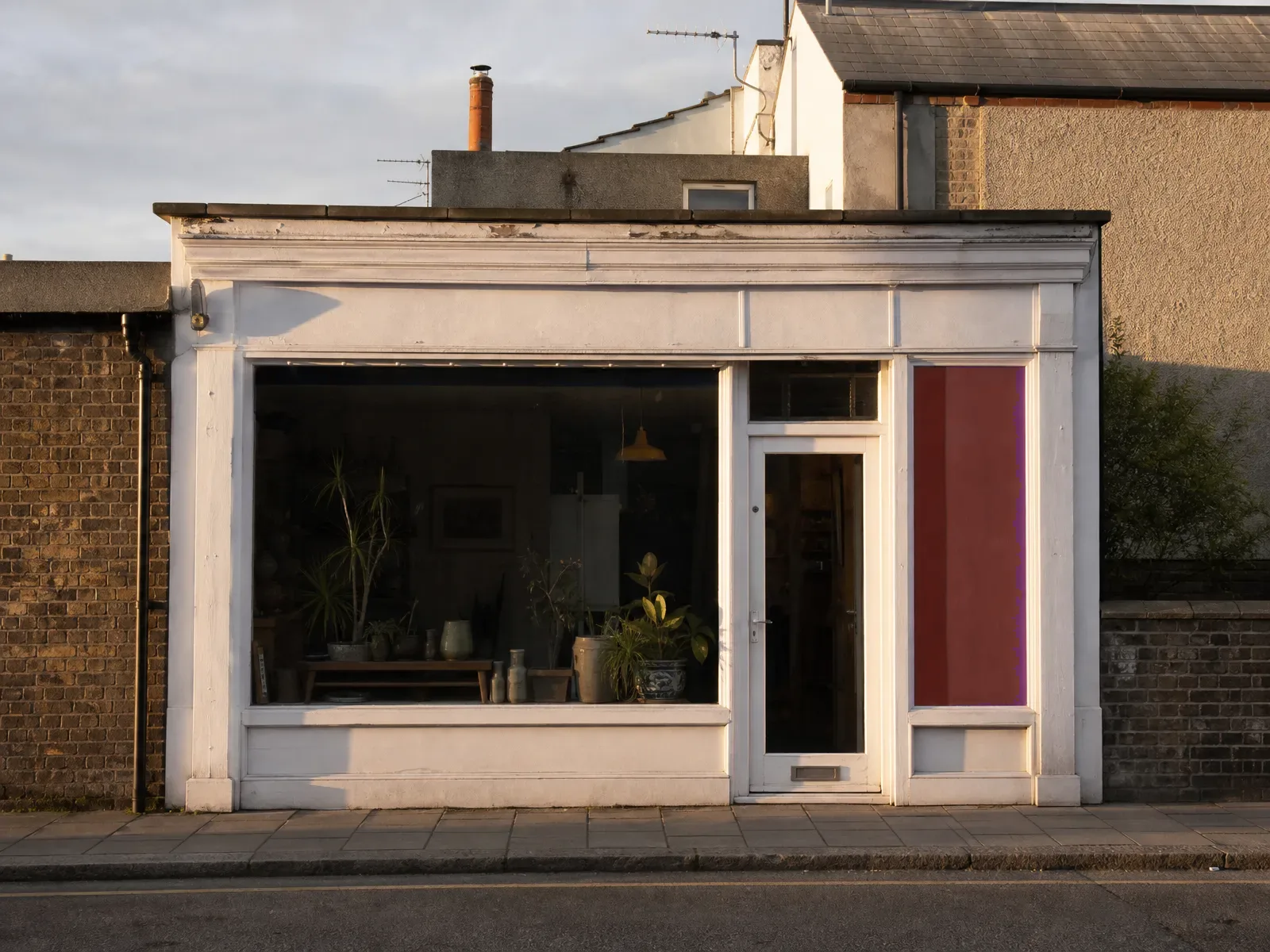 Small independent UK high-street shopfront at golden hour with a painted timber fascia and a red