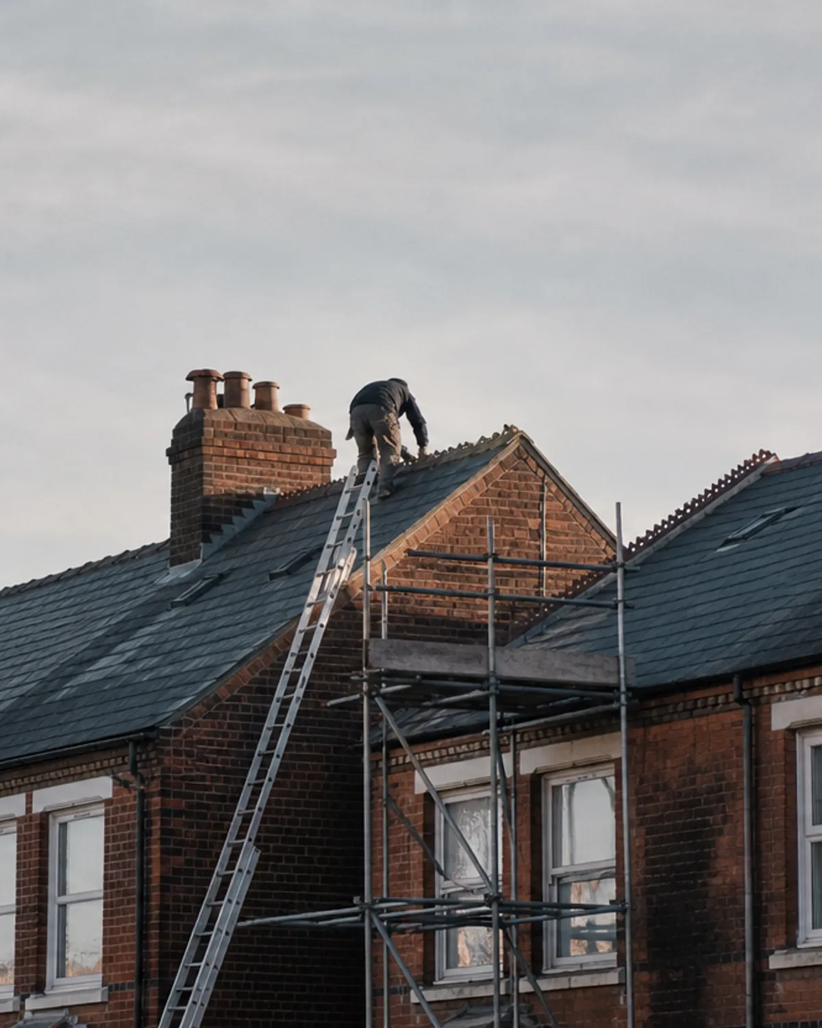 A roofer re-slating the ridge of a Victorian terrace from a scaffold